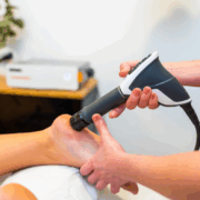 Someone performing shockwave therapy on a foot as a person is laying down